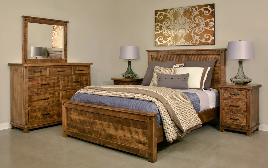 Handstone Adirondack bedroom set in wormy maple with a Sawmill Harvest finish, featuring a wood bed, matching dresser with framed mirror, and three-drawer nightstands. Warm cognac tones, distinctive natural wood grain, and dark metal hardware complete the rustic design.