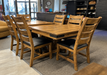 rustic solid maple dining table with a warm barley coloured finish and black metal corner bracket accents, with 6 matching ladderback chairs that have black upholstered seats