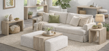 Bright, contemporary living room featuring a coordinated set of light wood accent tables, console tables, and coffee tables with clean waterfall-style silhouettes. The furniture is styled around a cream slipcovered sofa with a textured ottoman, woven baskets, neutral décor, and large windows that fill the space with natural light, creating a warm Scandinavian-inspired aesthetic.